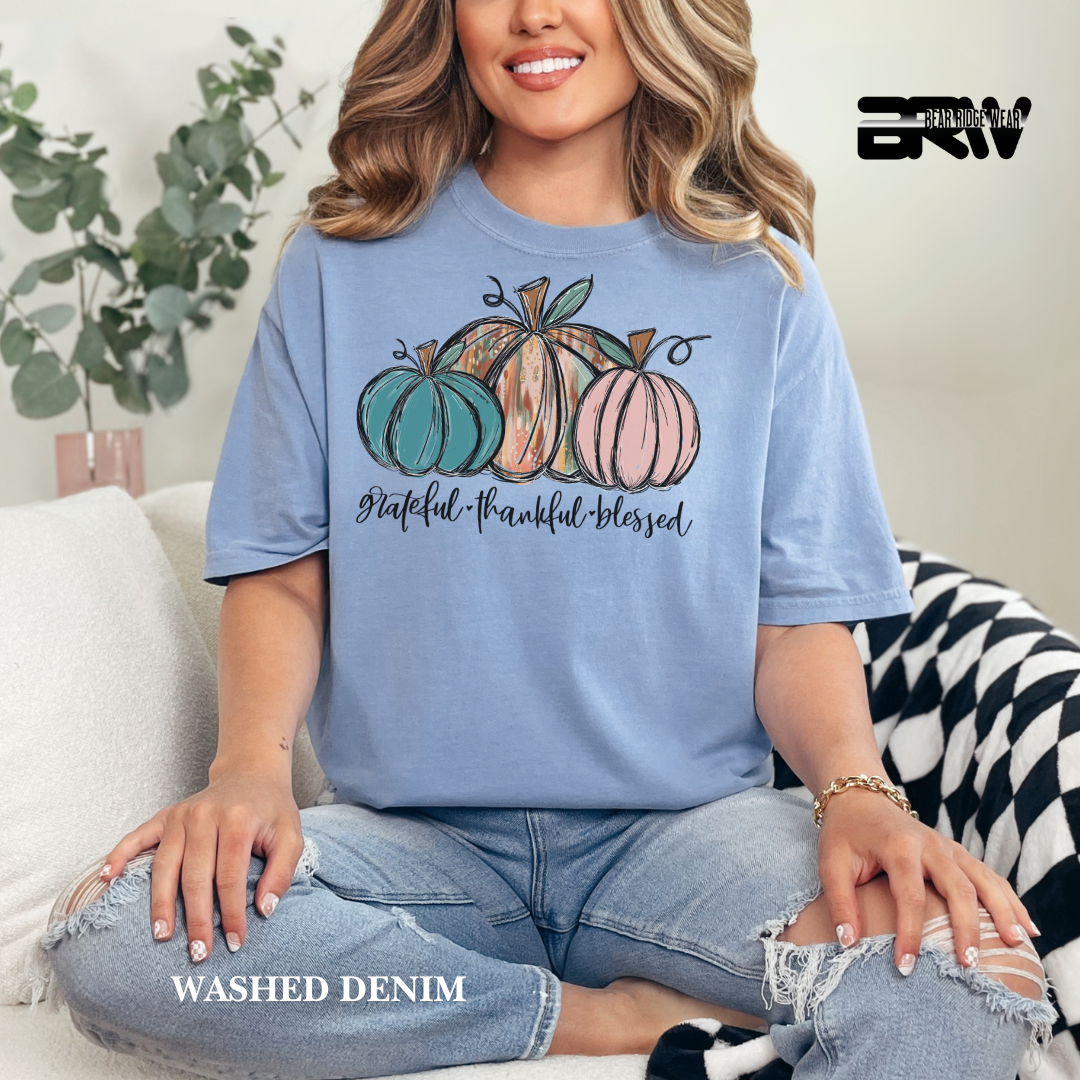 Woman wearing a blue t-shirt with pumpkins and text, sitting on a couch.
