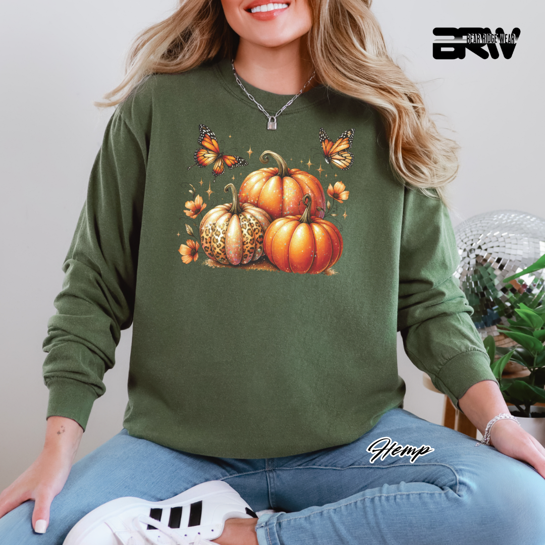 Person wearing a green sweatshirt with pumpkins and butterflies design, sitting on a white surface.