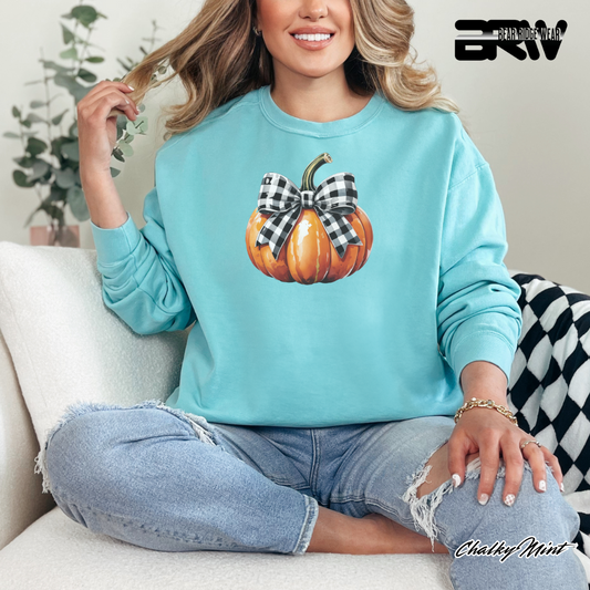 Woman wearing a light blue sweatshirt with a pumpkin design, sitting on a couch.