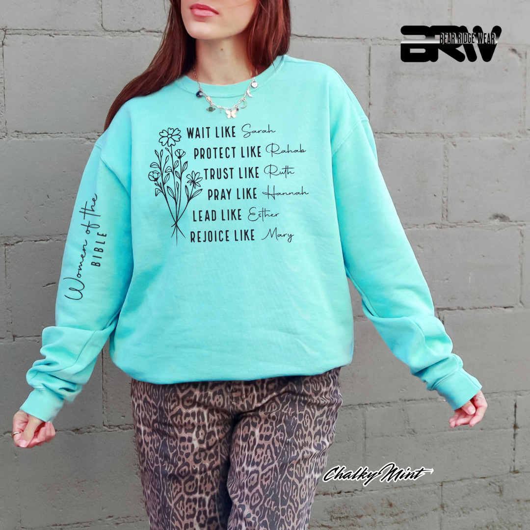 Person wearing a turquoise sweatshirt with text and graphics against a gray wall.
