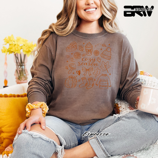 Woman wearing a brown sweatshirt with autumn-themed graphics, sitting on a couch.