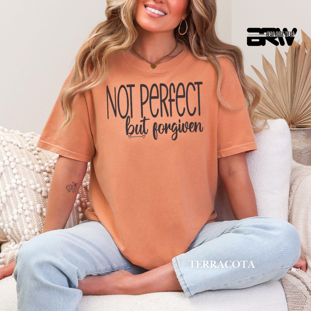 Woman wearing a terracotta t-shirt with 'Not perfect but forgiven' text, sitting on a couch.