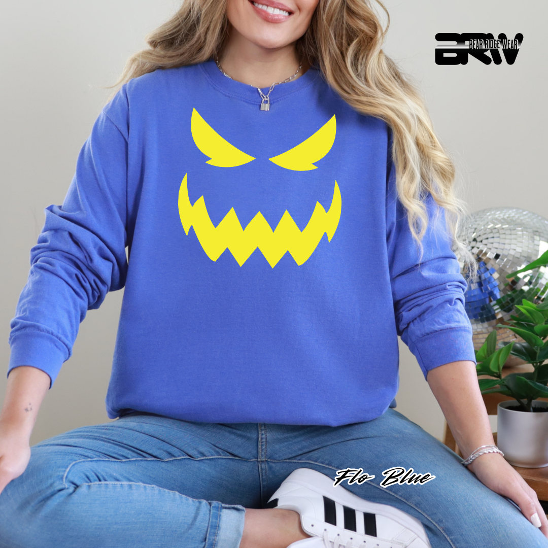 Person wearing a blue sweatshirt with a yellow angry face design, sitting indoors.