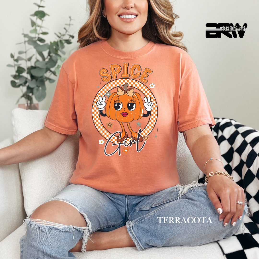 Person wearing a terracotta-colored t-shirt with a pumpkin graphic and text, sitting on a couch.