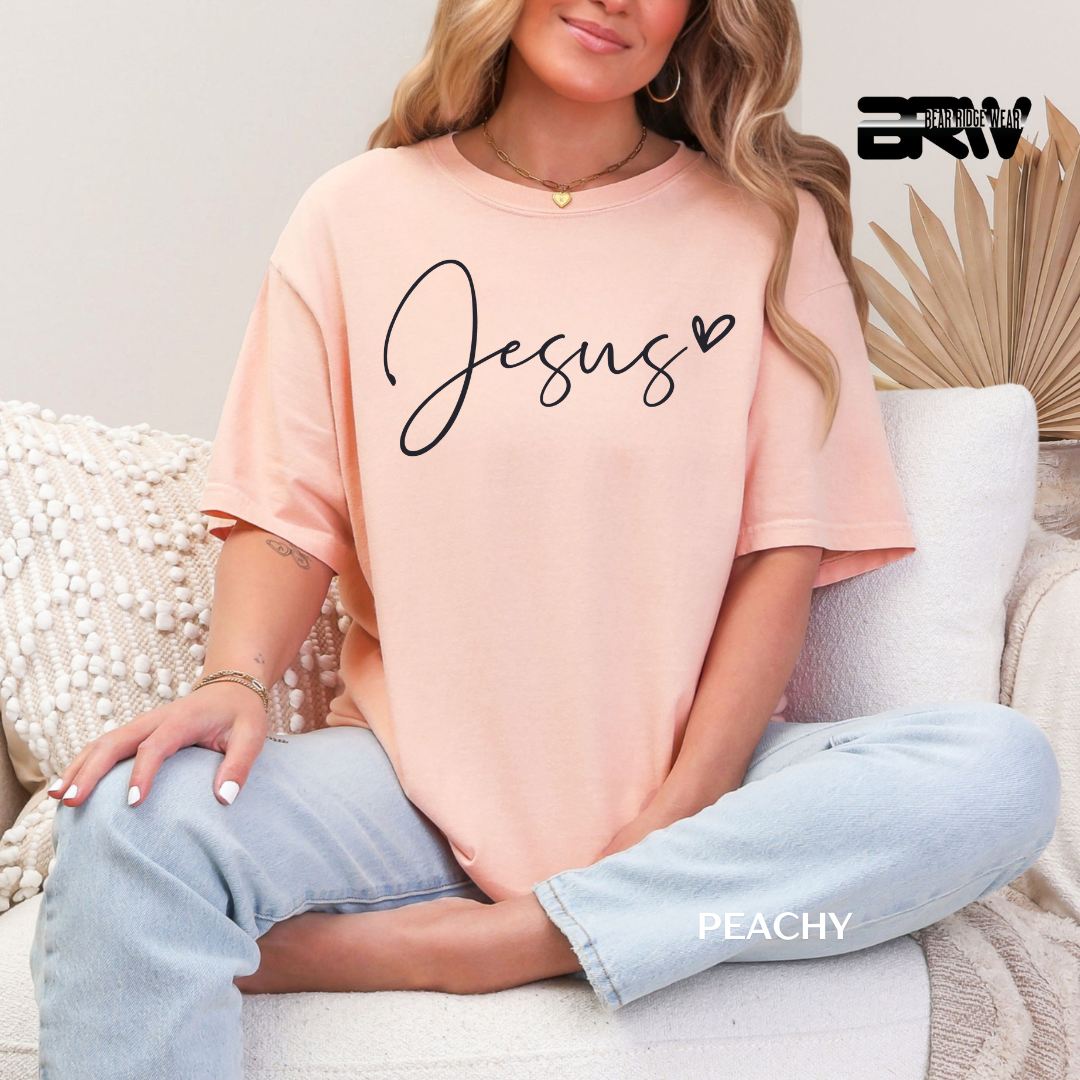 Person wearing a peach-colored t-shirt with 'Jesus' printed on it, sitting on a couch.