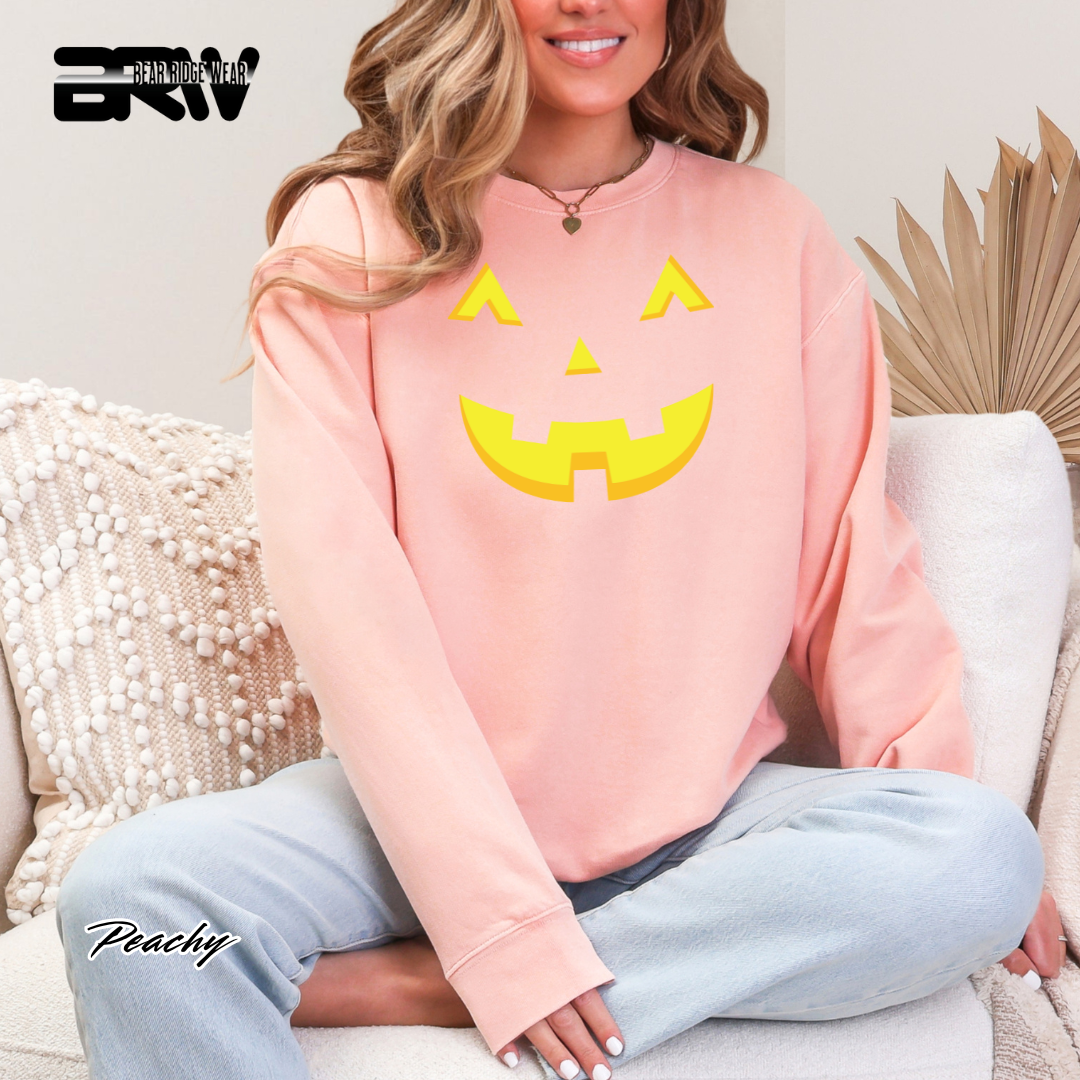 Person wearing a pink sweatshirt with a yellow pumpkin face design, sitting on a couch.