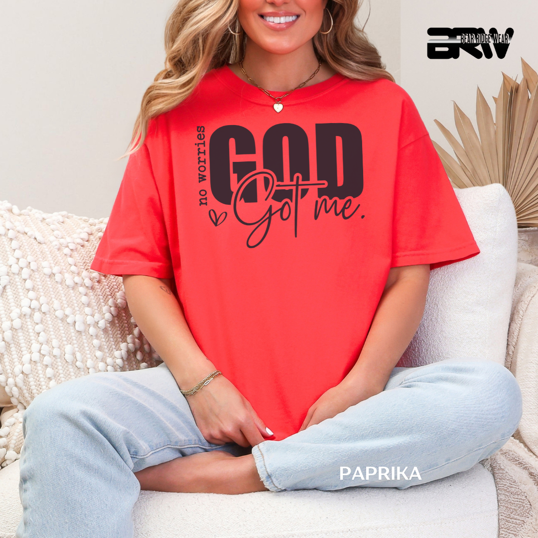 Person wearing a red t-shirt with 'God got me' text, sitting on a couch.