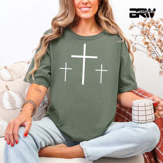 Woman wearing a green t-shirt with cross designs, sitting on a couch holding a mug.