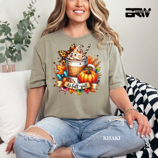 Woman wearing a khaki t-shirt with a fall-themed design, sitting on a couch.