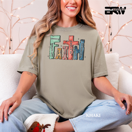 Woman wearing a khaki t-shirt with colorful text design, sitting on a couch. COOLOFUL FAITH TEE