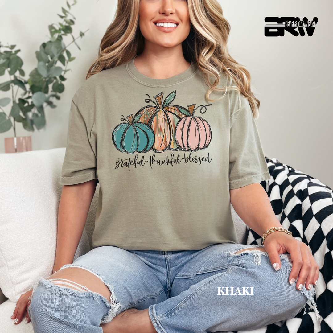 Woman wearing a khaki t-shirt with pumpkins and text, sitting on a couch.