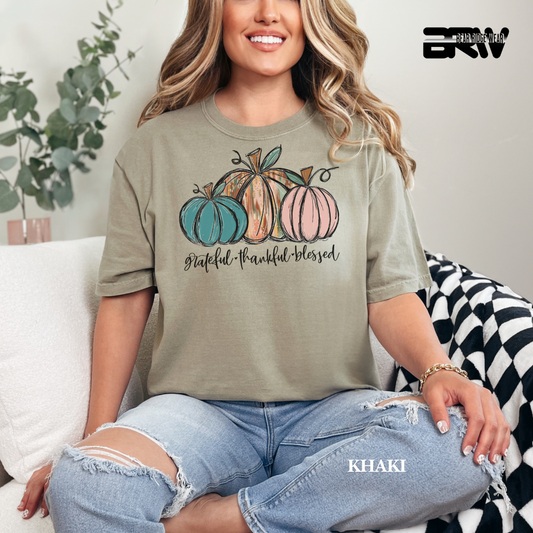 Woman wearing a khaki t-shirt with pumpkins and text, sitting on a couch.