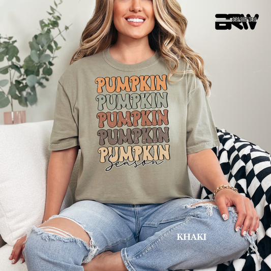 Woman wearing a khaki t-shirt with 'Pumpkin Season' text, sitting on a couch.
