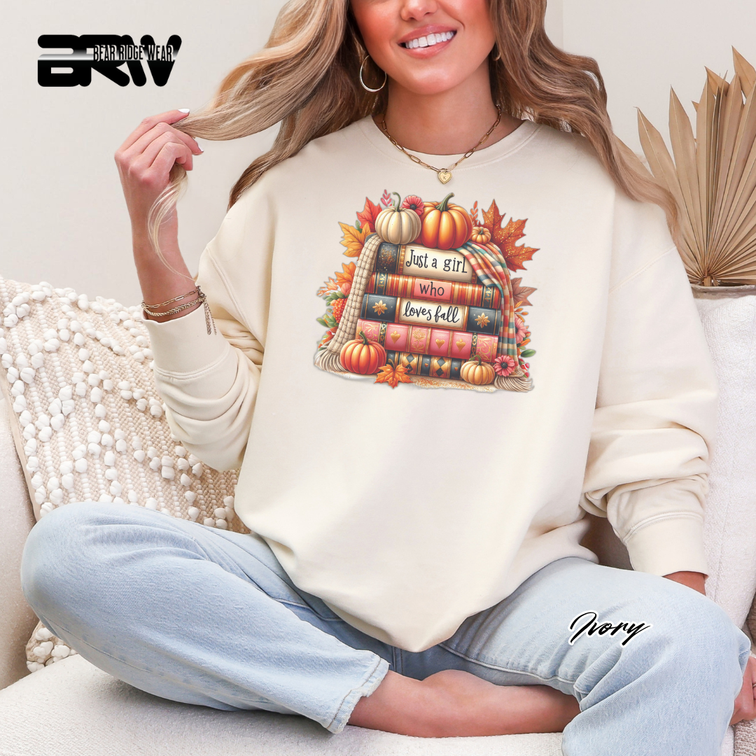 Woman wearing a cream sweatshirt with a fall-themed design, sitting on a couch.
