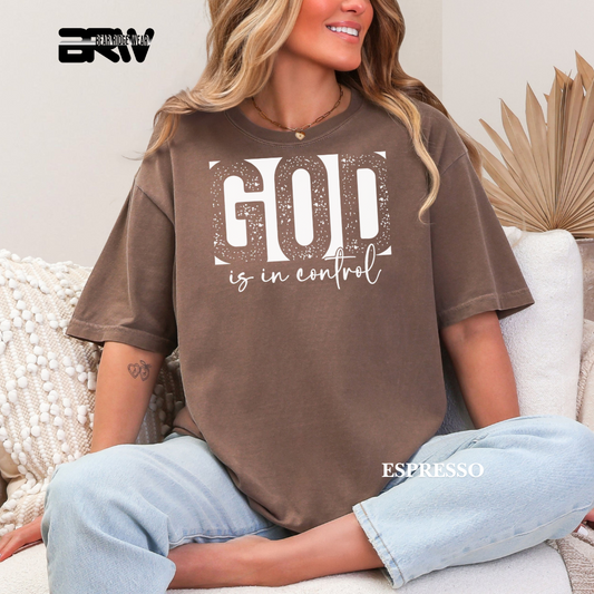 Person wearing a brown t-shirt with 'GOD is in control' text, sitting on a couch.